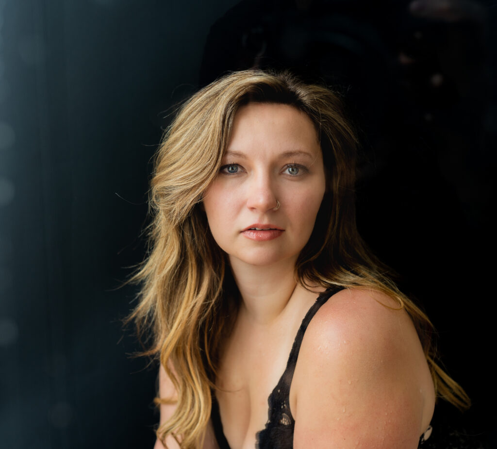 girl with blue green eyes and blonde hair staring at the camera gently with al all black background taken in medina ohio boudoir