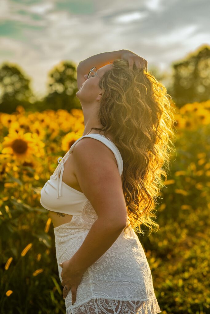 girl in white dress in sunflower field with sun shining through her hair at medina sunflower farm in medina ohio 