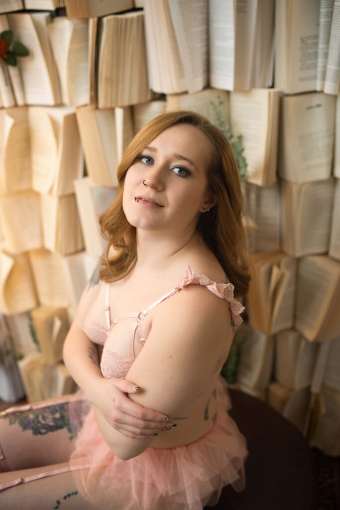 woman in pink top giving herself a hug while sitting in front of a wall of books and staring at the camera in medina, ohio